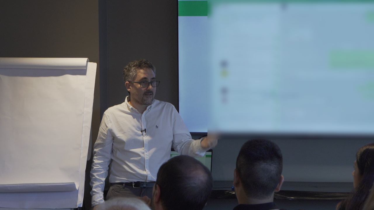 Francisco Santolo en clase, señalando una pantalla con un agente de mensajería en funcionamiento, frente a los asistentes.