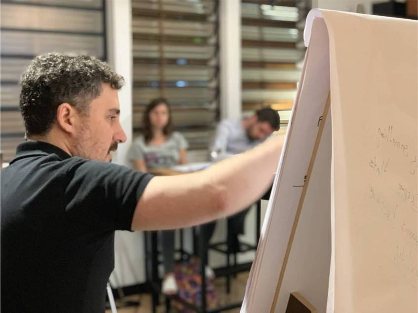 Francisco Santolo escribiendo en un rotafolio mientras dos participantes trabajan detrás.